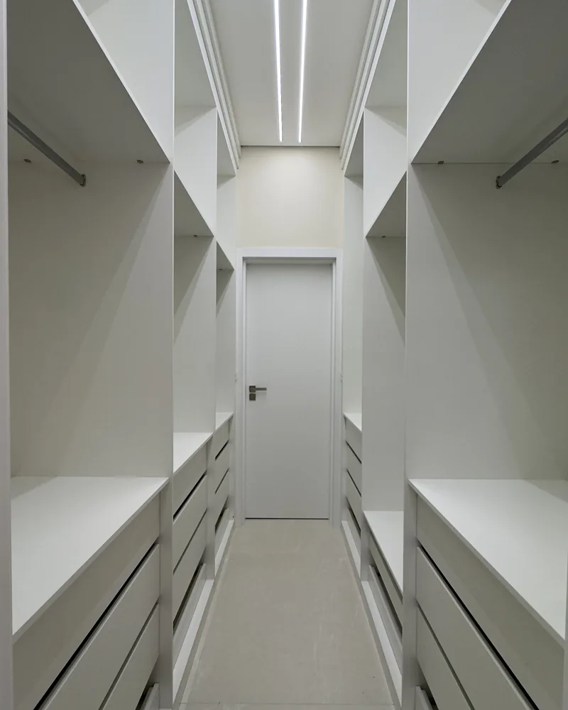 Closet planejado em branco, com prateleiras, gaveteiros e iluminacao em fita de LED no teto