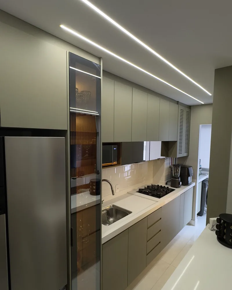 Cozinha corredor em tom fendi, com cristaleira espelhada, cooktop e fita de LED no teto